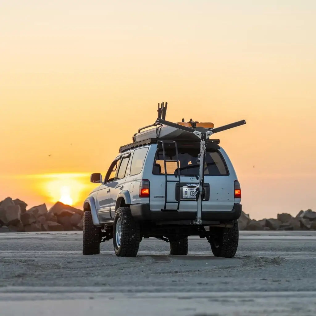 White wagon at sunset on a beach with a kayak carried on the roof by the Will-I Kayak loader
